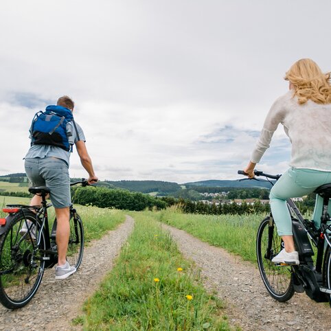 Ein Paar im Urlaub im Sauerland beim Radfahren. Im Hintergrund ist ein Wald.