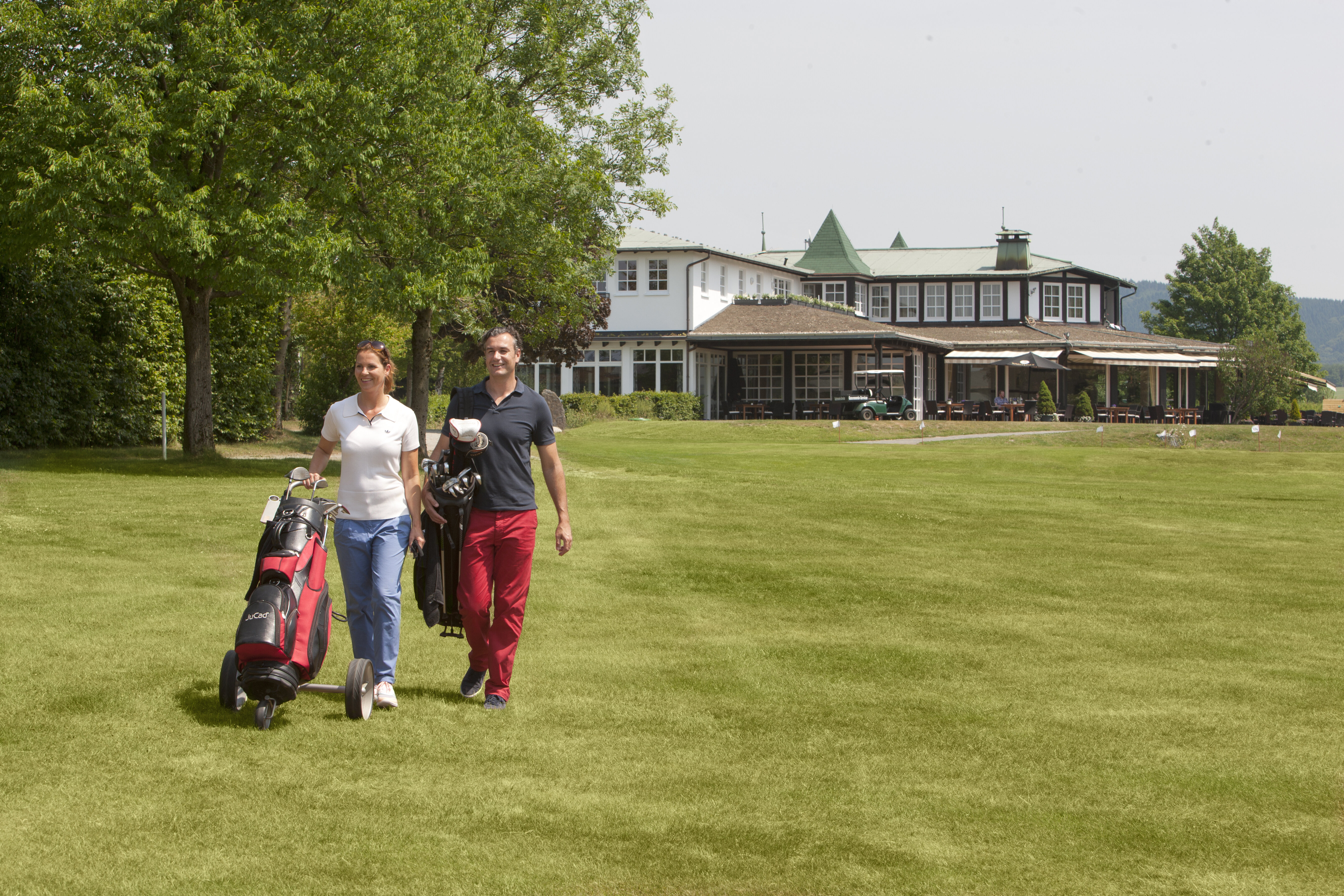 Pärchen auf dem Golfplatz im Sauerland mit Golfausrüstung und dem Restaurant im HIntergrund