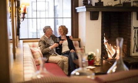 Ein älteres Pärchen genießt ihren Urlaub im Sauerland mit einem Glas Wein vor dem gemütlichen Kaminfeuer 