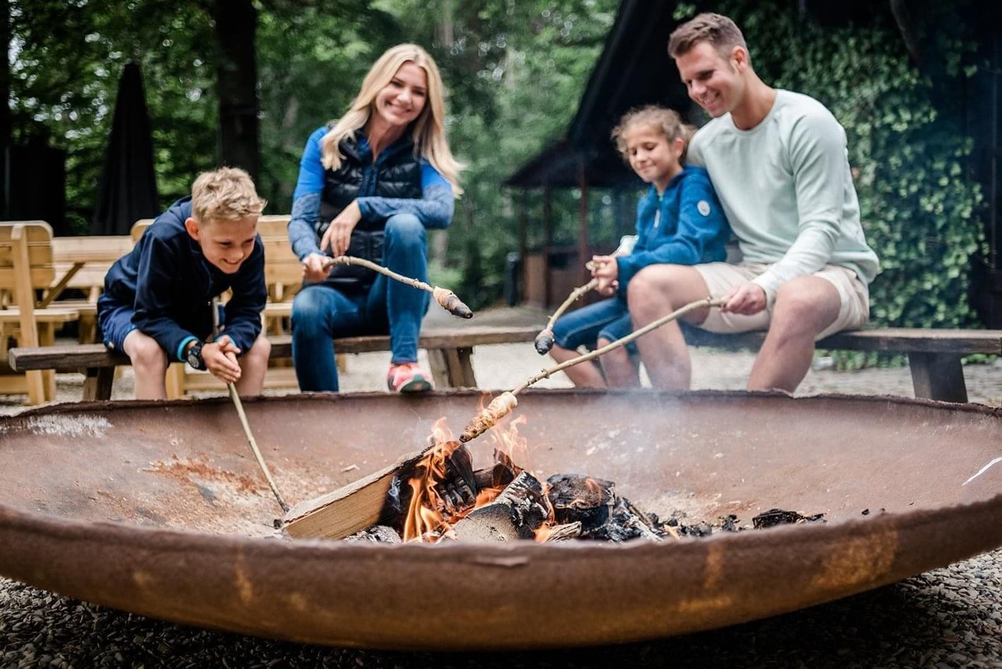 Eine Familie sitzt lachend mit Stockbrot am Feuer und freut sich über ihren gemeinsamen Familienurlaub in NRW