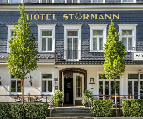 Vorderansicht des Hotel Störmann mit Eingang, Terrasse und zwei Bäumen vor der Fassade.