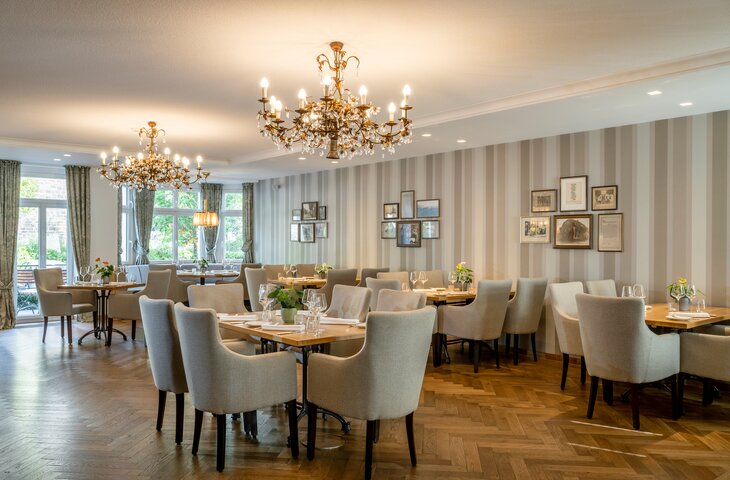 Veranstaltungsraum im Hotel Störmann im Sauerland mit Kronleuchtern, gestreifter Wandverkleidung, Bildergalerie und festlich gedeckten Tischen.