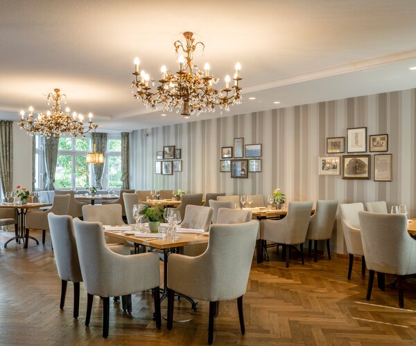 Veranstaltungsraum im Hotel Störmann im Sauerland mit Kronleuchtern, gestreifter Wandverkleidung, Bildergalerie und festlich gedeckten Tischen.