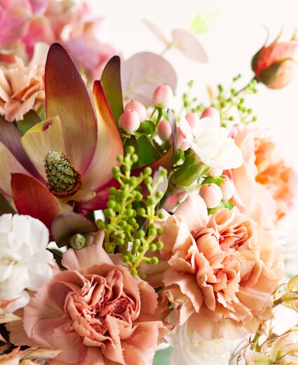 Blumenbouquet mit pfirsichfarbenen, rosafarbenen und weißen Blüten, grünem Laub und kleinen Knospen vor hellem Hintergrund