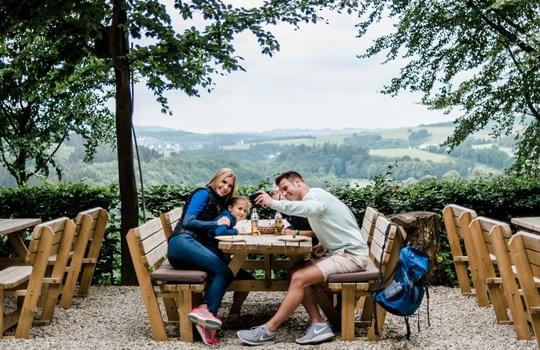 Eine Familie sitzt an einem Tisch im Außenbereich der Knollenhütte vom Hotel Deimann.
